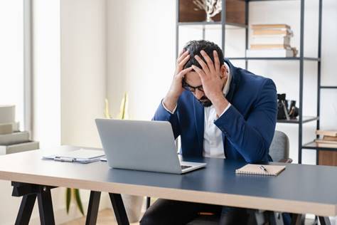 A frustrated businessman sits at his desk with his head in his hands.